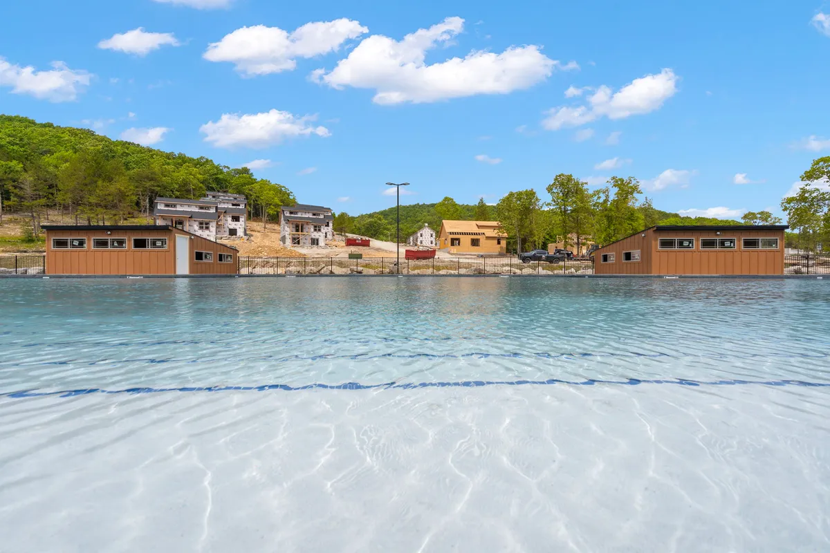A scenic waterfront with clear, tranquil water bordered by lush greenery and waterfront buildings. Boating, fishing, and nature walks are implied, with sunset views casting a peaceful mood over the setting.