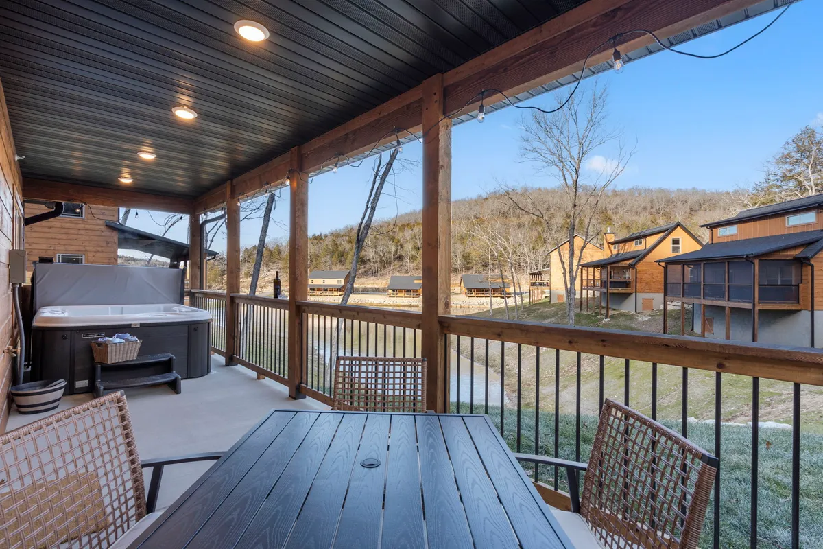A private outdoor deck featuring a bubbling hot tub and dining table, set against a backdrop of rolling mountains. The serene setting is perfect for unwinding after an active day.
